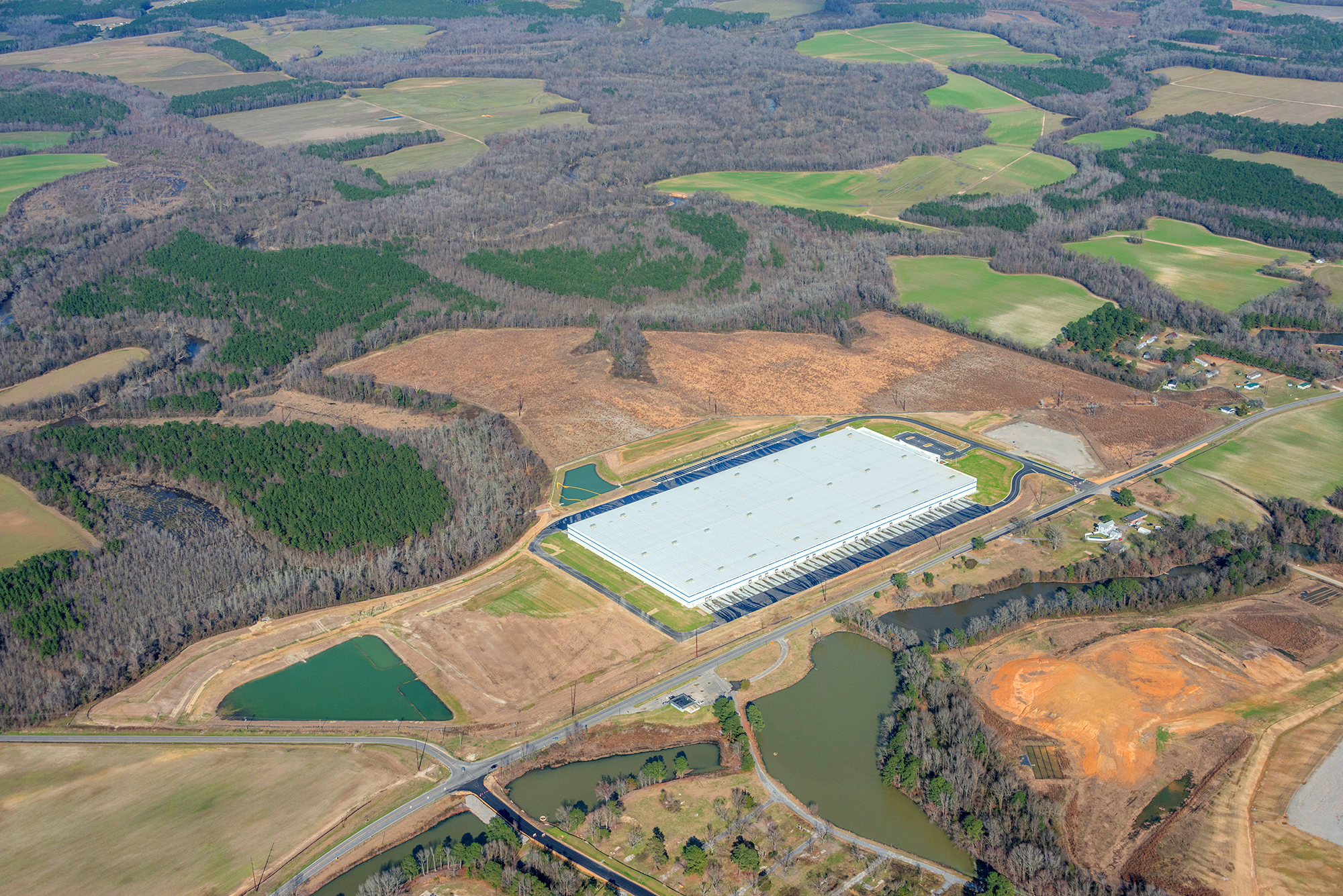 An aerial shot of a large distribution warehouse, access roads, and detention ponds